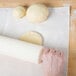 A hand rolling white dough with a white rolling pin cover on a white surface.