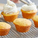 A person using a pastry brush to frost a group of cupcakes.