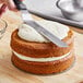 A person's hand cutting a Gold Medal carrot cake with cream cheese frosting.