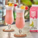 Two glasses of Island Oasis Rum Runner with fruit garnish and a box of Island Oasis Rum Runner juice on a table.