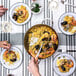 A de Buyer paella pan filled with rice, seafood, and a spoon on a table with a glass of wine.