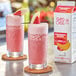 Two glasses of pink strawberry banana drinks on a table with fruit on the rim.