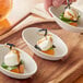 A hand holding a spoon with food over a white EcoChoice natural bagasse appetizer bowl.