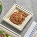 A EcoChoice natural bagasse square plate of food on a table.