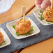 A person holding a toothpick on a small EcoChoice natural bagasse blend square appetizer plate.