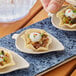 A person holding a small tortilla with food on a natural bagasse leaf appetizer plate.