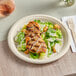 A plate of food on a table with EcoChoice Natural Bagasse Blend plates holding salad and chicken.