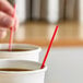 A red and white unwrapped coffee stirrer placed in a paper cup of coffee.