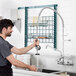 A man using an Equip by T&S wall-mounted pre-rinse faucet to wash dishes in a professional kitchen.