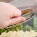 A hand holding a clear Cambro Deli Crock lid over a container of food.