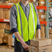 A man wearing a Lavex lime green high visibility safety vest holding a stack of cardboard boxes.