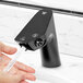 A person's hand with water running from a black Waterloo dual-sensor faucet.