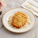 A WNA Comet ivory plastic plate with gold accent bands holding chicken and rice on a table with a glass of liquid.