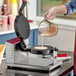 A person wearing a glove pouring liquid into an Estella commercial waffle cone maker.