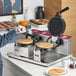 A person making waffles on an Estella double waffle maker on a counter.