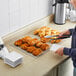 A person using tongs to place croissants in a wire basket.