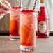 A hand holding a drink with a straw and a cherry next to a bottle of Rose's Grenadine syrup.