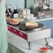 A person using an Estella double crepe maker to make pancakes on a griddle in a professional kitchen.