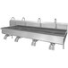 A Sani-Lav stainless steel wall mounted multi-station hands-free sink with knee-operated faucets.