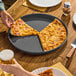 A round, straight-sided, hard coat anodized aluminum pizza pan with a partially eaten pizza on it.