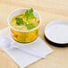 a cup of soup with a spoon and a plastic lid