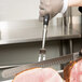 A hand using a Winco 12" Forged Pot Fork to hold a piece of meat while cutting it with a knife.
