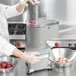 A woman in a professional kitchen using a Waring food processor to chop potatoes.