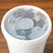 A Dart translucent plastic lid with a straw slot on a white foam cup with a drink inside.