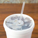 A white Dart foam cup with a straw and a translucent lid with a straw slot.