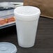 A white plastic Dart cup with a translucent lid and straw slot on a table.