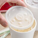 A hand putting a Dart Translucent plastic lid on a plastic cup.