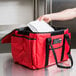 A person putting a white container into a red Rubbermaid insulated delivery bag.