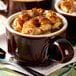 A Tuxton caramel and eggshell china soup mug filled with food on a plate with a spoon.