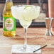 A margarita glass with a drink in it and a bottle of Rose's Sweetened Lime Juice on a table in a Mexican restaurant.