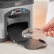 A hand using a KleanTake ramp to dispense a lid onto a plastic cup.