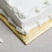 A white cake with frosting on a gold Enjay quarter sheet cake board.