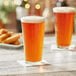 Two Acopa Select mixing glasses filled with beer on a table.