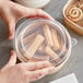 A hand holding a container of cinnamon rolls with a Choice polypropylene lid.