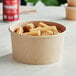 A round Kraft paper take-out container filled with churros on a table.