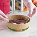 A hand in gloves placing a EcoChoice PLA lid on a plastic container of food.