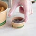 A hand in a glove reaching for a EcoChoice compostable lid on a container of food.