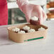 A person putting a brownie with white frosting into an EcoChoice brown rectangular take-out container.