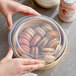 A hand reaching for a round plastic lid on a container of macarons.