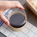 A hand using a Choice 4 oz. plastic take-out lid to hold a container of liquid.