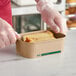 A person in gloves holding a piece of food in a rectangular cardboard container.