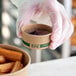 A hand holding an EcoChoice round brown take-out container filled with brown liquid.