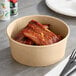 A Choice kraft paper bowl filled with food on a table with a fork.