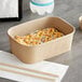 A rectangular Kraft paper take-out container with sushi inside on a table.