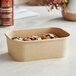 A close-up of a brown Choice rectangular paper take-out container of muffins on a table.