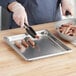 A person using tongs to serve sausages from a Vollrath stainless steel steam table pan.